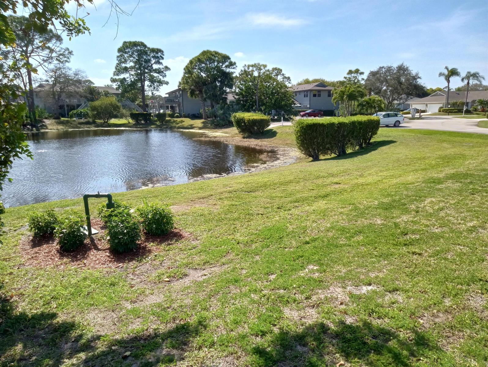 A pond sits in front of a grassy lawn with trimmed hedges and residential buildings — 630 E Pointe Ct SW, Vero Beach FL 32962, VERO BEACH, FL