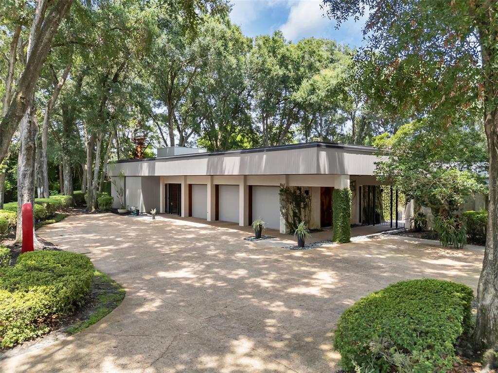 A modern single-story house with a multi-car garage and a large paved driveway under trees — 111 SAND PINE LANE, LONGWOOD, FL