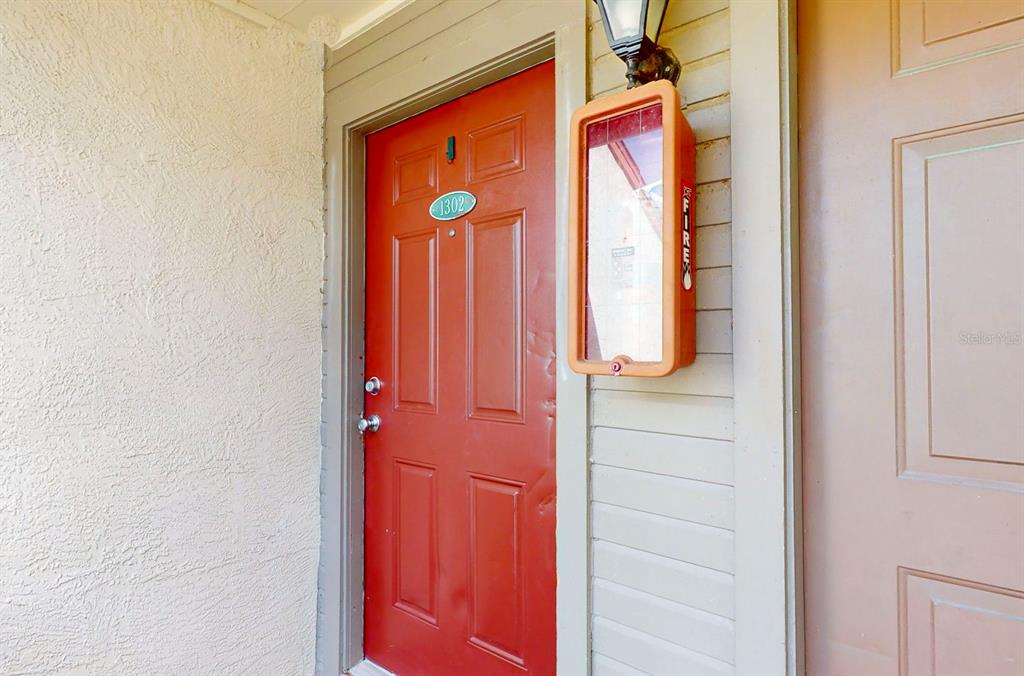 A red apartment door numbered 1302 sits next to a wall-mounted fire extinguisher cabinet — 10265 GANDY BOULEVARD N UNIT 1302, ST PETERSBURG, FL