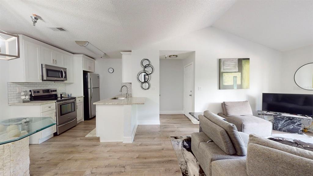 An open-concept kitchen and living area with white cabinets, stainless appliances, and wood-look flooring — 10265 GANDY BOULEVARD N UNIT 1302, ST PETERSBURG, FL