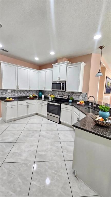 A kitchen features white cabinets, dark countertops, stainless steel appliances, and light-colored tile flooring — 11114 HARTFORD FERN DRIVE, RIVERVIEW, FL