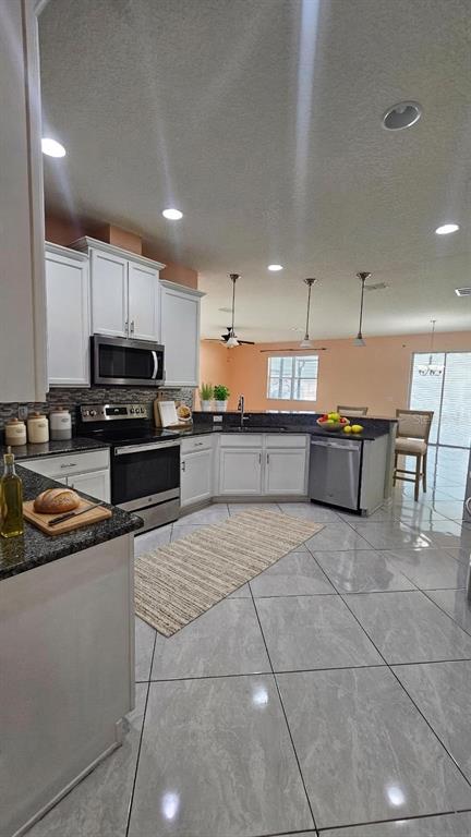 A kitchen features white cabinets, stainless steel appliances, granite countertops, and large gray floor tiles — 11114 HARTFORD FERN DRIVE, RIVERVIEW, FL