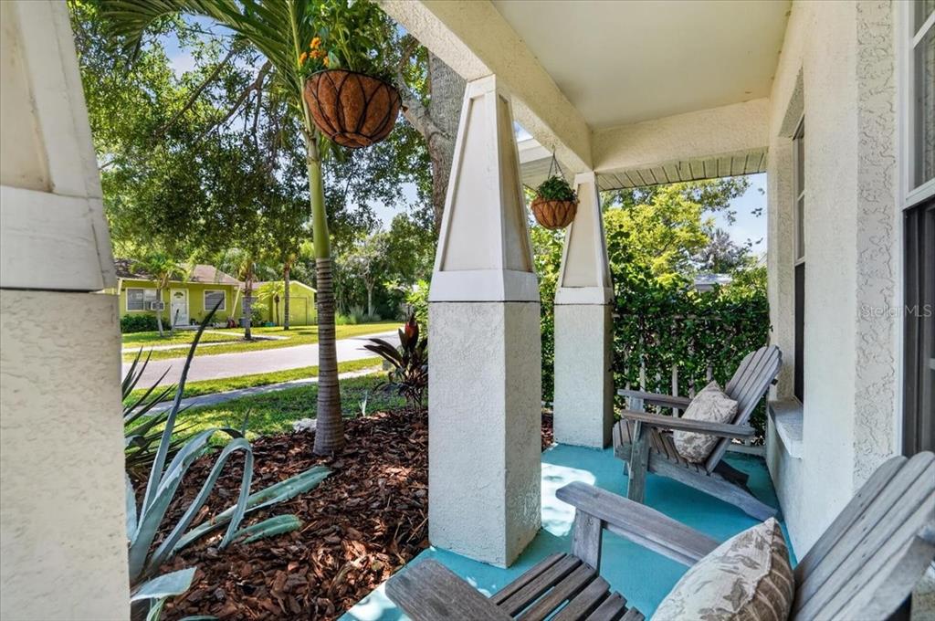 A covered porch features two wooden chairs, hanging planters, and views of a neighborhood street — 5109 17TH AVENUE S, GULFPORT, FL