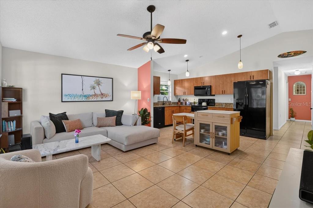 An open-concept living room and kitchen feature tile flooring, a ceiling fan, and wooden cabinets — 5109 17TH AVENUE S, GULFPORT, FL