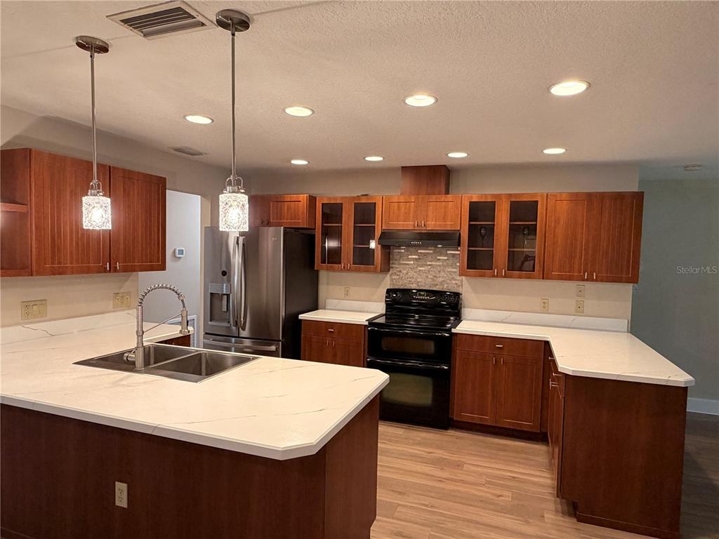 A kitchen features wood cabinets, white countertops, stainless steel appliances, and a central island — 521 HIAWATHA AVENUE, INVERNESS, FL