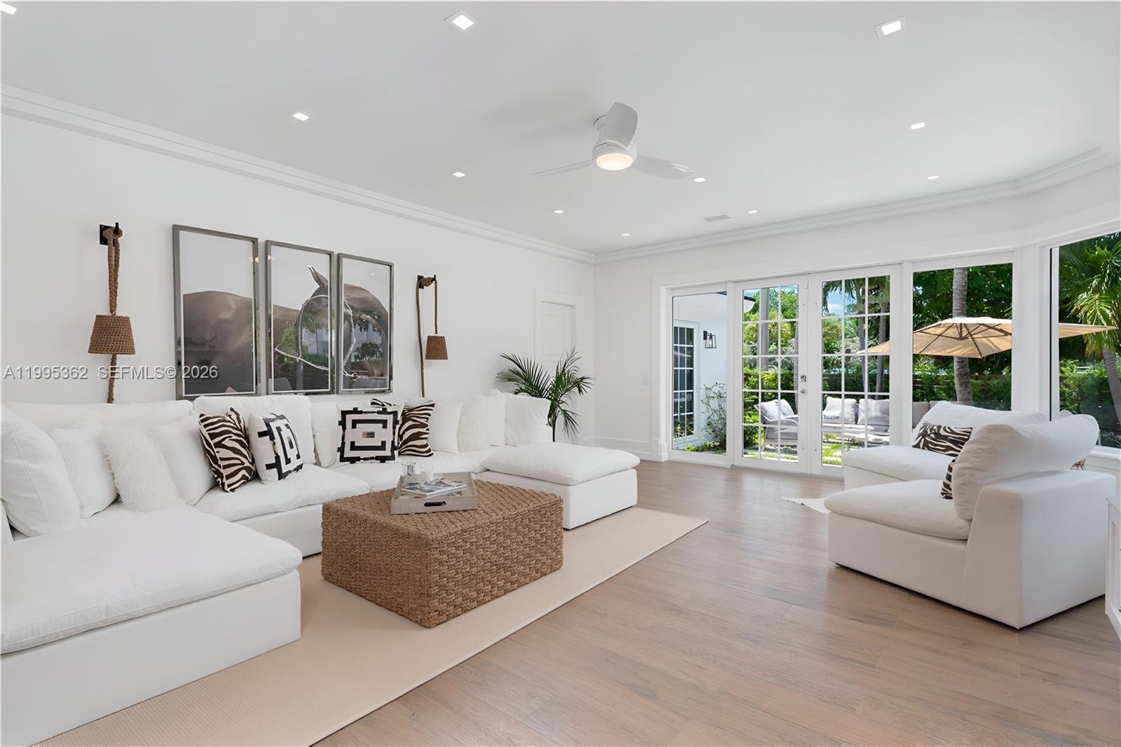 A bright living room features a large white sectional, a woven coffee table, and glass doors — 2575 Pine Tree Dr, Miami Beach FL 33140, MIAMI BEACH, FL