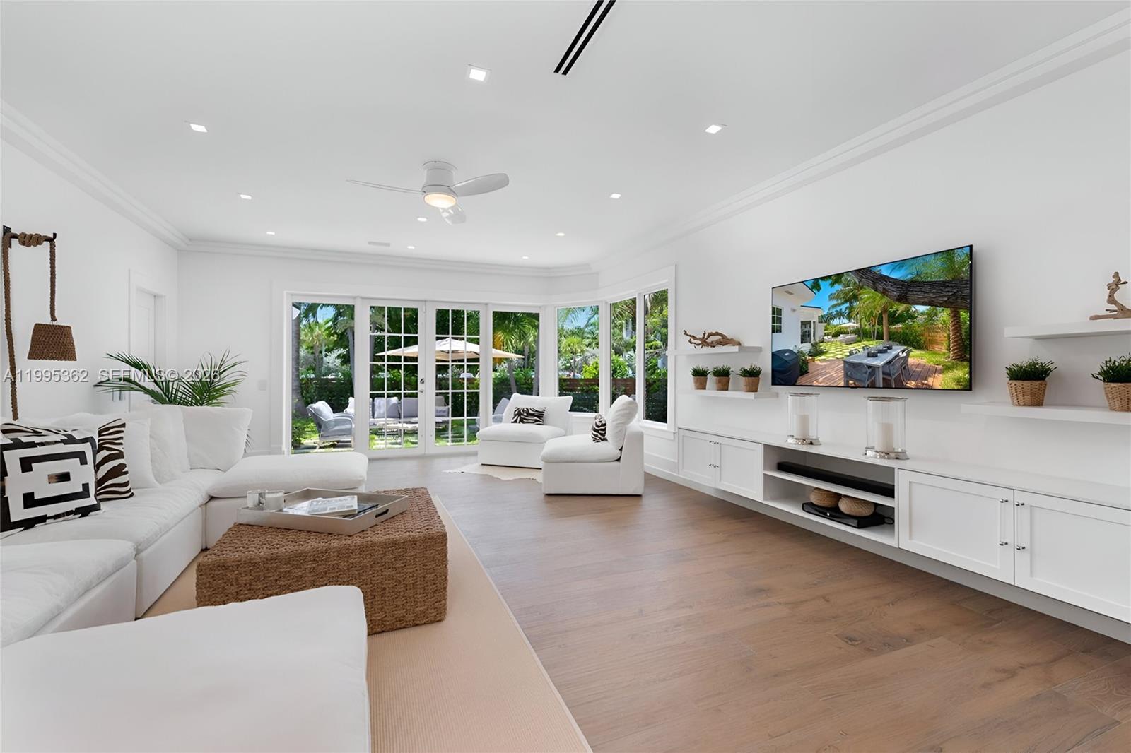 A bright living room features white furniture, a woven coffee table, and large glass doors — 2575 Pine Tree Dr, Miami Beach FL 33140, MIAMI BEACH, FL