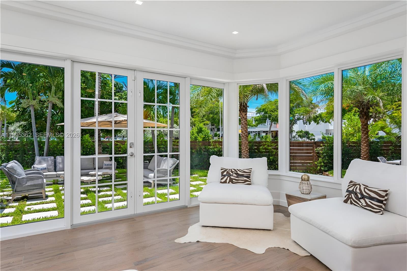 A sunroom with white furniture, wood flooring, and glass doors opening to a patio — 2575 Pine Tree Dr, Miami Beach FL 33140, MIAMI BEACH, FL