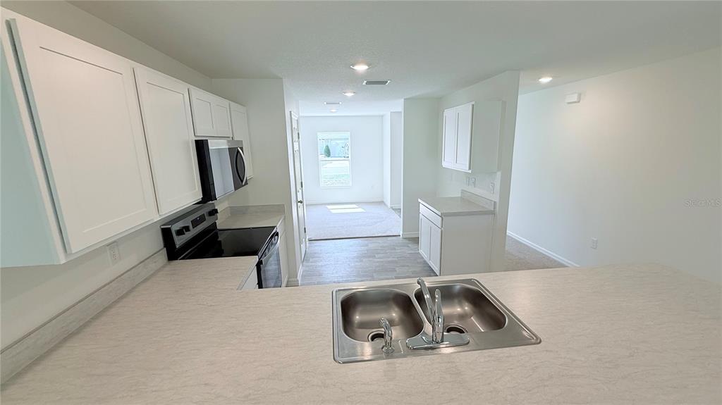 A kitchen with white cabinets, laminate countertops, and a double-basin sink overlooks an adjacent room — 29 PERKINS LANE, PALM COAST, FL