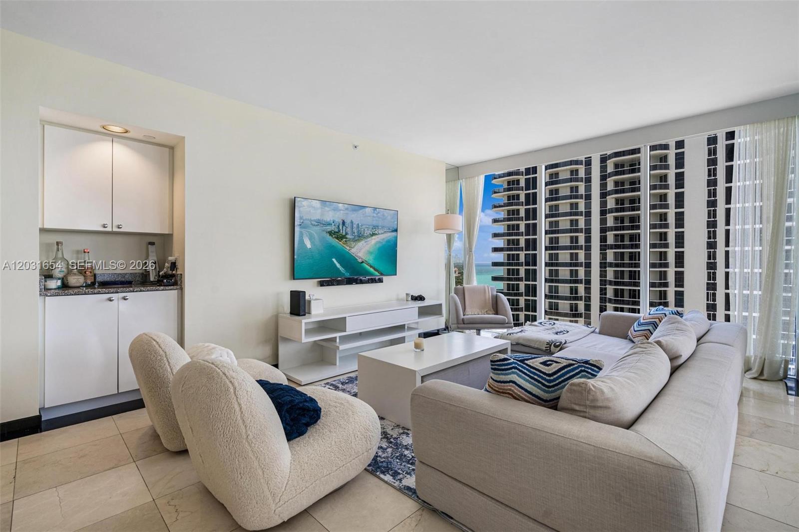 A living room features a white media console, a sectional sofa, and floor-to-ceiling windows — 4779 Collins Ave # 2305, Miami Beach FL 33140, MIAMI BEACH, FL