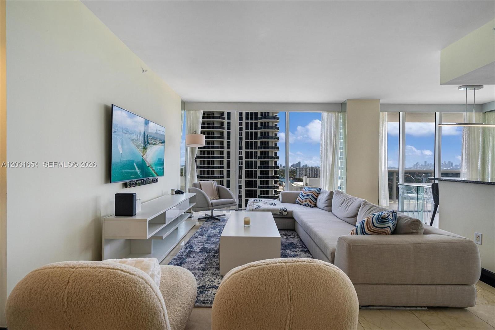 A living room features a sectional sofa, a television, and floor-to-ceiling windows with city views — 4779 Collins Ave # 2305, Miami Beach FL 33140, MIAMI BEACH, FL