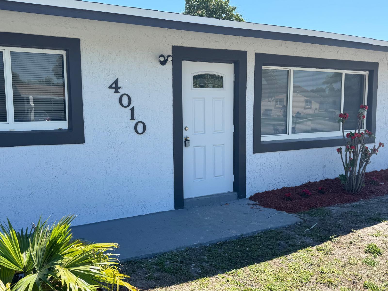 The exterior of a white house features a front door, address numbers, and a window — 4010 NE 6th Avenue, Deerfield Beach FL 33064, DEERFIELD BEACH, FL