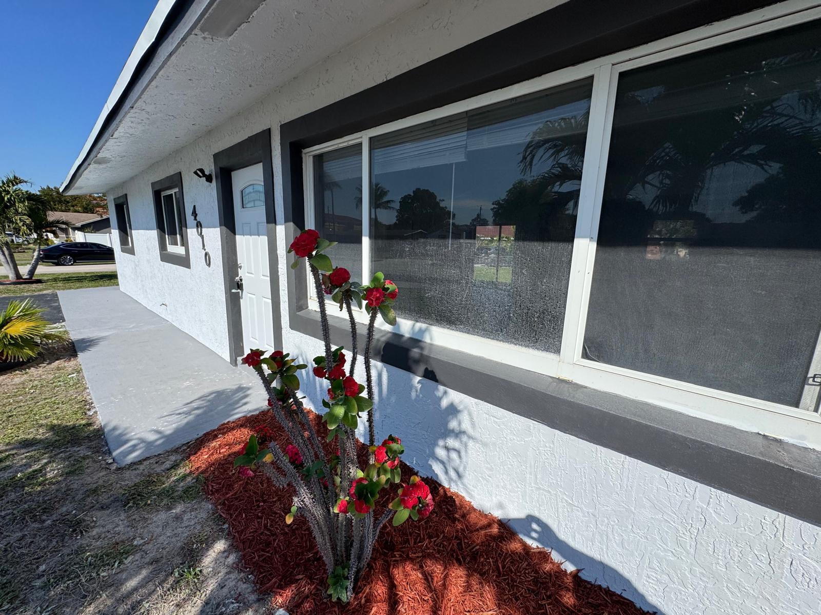 A white house exterior features a front door, a large window, and a flowering cactus — 4010 NE 6th Avenue, Deerfield Beach FL 33064, DEERFIELD BEACH, FL
