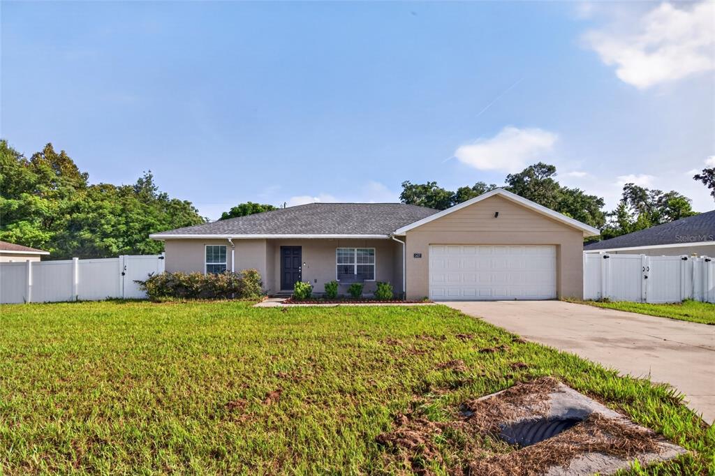 A single-story house with a beige exterior, a two-car garage, and a white vinyl fence — 1437 NE 161ST PLACE, CITRA, FL
