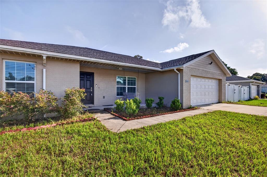 A single-story house with a beige stucco exterior, a dark front door, and a two-car garage — 1437 NE 161ST PLACE, CITRA, FL