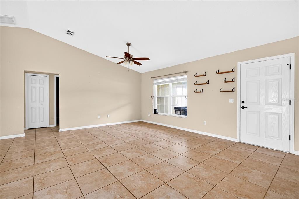 An empty living room features beige walls, tiled flooring, a ceiling fan, and a front door — 1437 NE 161ST PLACE, CITRA, FL