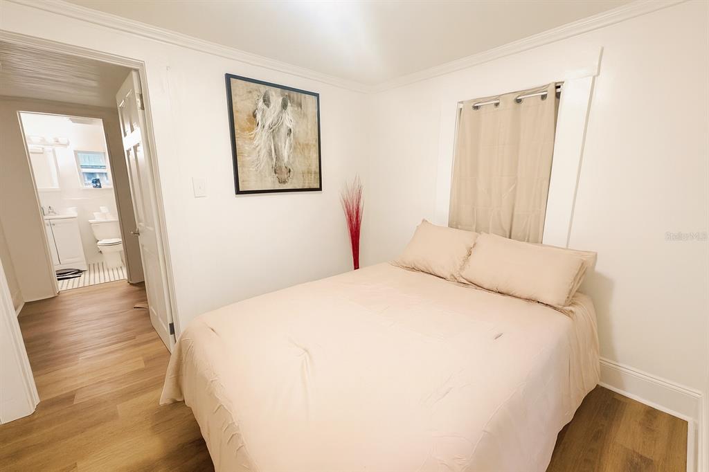 A bedroom with light wood flooring, a bed, a horse painting, and an adjacent bathroom — 7105 N 10TH STREET, TAMPA, FL