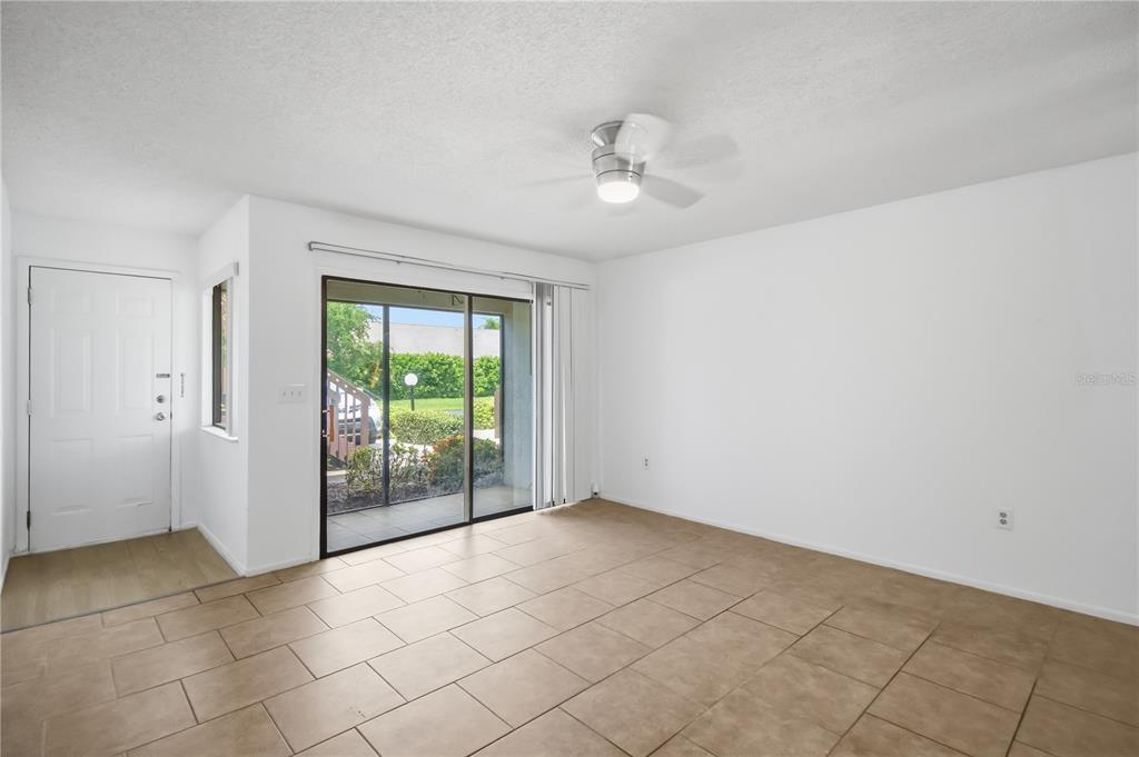An empty room features tan tile flooring, white walls, a ceiling fan, and sliding glass doors — 2715 72ND STREET COURT W, BRADENTON, FL