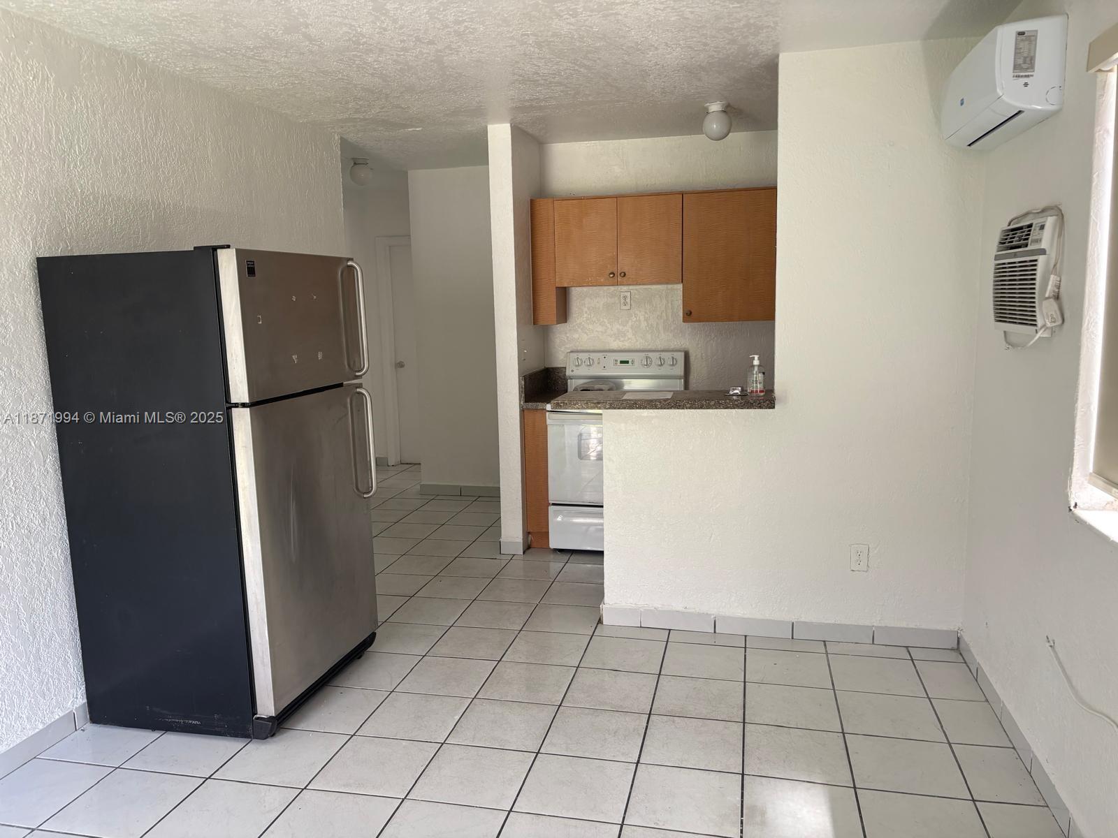 A kitchen area features a stainless steel refrigerator, wooden cabinets, and white tiled flooring — 5100 NW 23rd Ave # 1, Miami FL 33142, MIAMI, FL