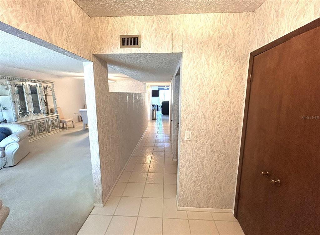A tiled hallway leads past a living room with wallpaper and a brown door — 2170 AMERICUS BOULEVARD S UNIT 57, CLEARWATER, FL
