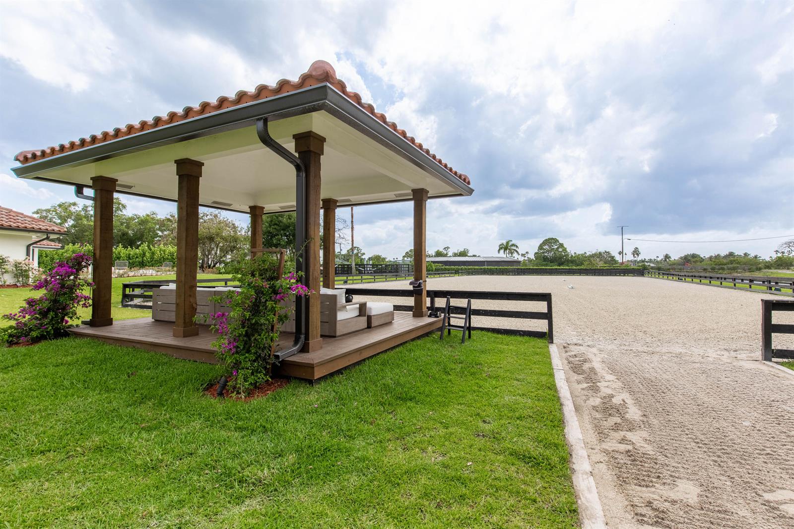 A covered wooden gazebo with outdoor seating sits beside a sand riding arena — 14794 Rolling Rock Place, Wellington FL 33414, WELLINGTON, FL