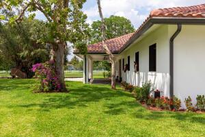 A white horse stable with a red tile roof sits beside a grassy lawn — 14794 Rolling Rock Place, Wellington FL 33414, WELLINGTON, FL