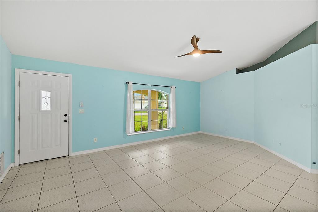 An empty room with light blue walls, tiled flooring, a ceiling fan, and a front door — 34 BEAVERDAM LANE, PALM COAST, FL