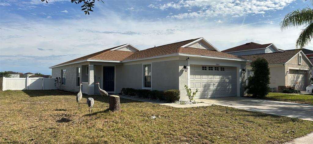 A single-story house with a tan stucco exterior, a two-car garage, and three cranes on the lawn — 12602 EVINGTON POINT DRIVE, RIVERVIEW, FL