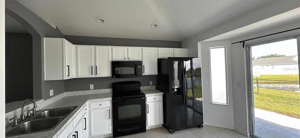 A kitchen features white cabinets, dark countertops, black appliances, and a sliding glass door — 12602 EVINGTON POINT DRIVE, RIVERVIEW, FL