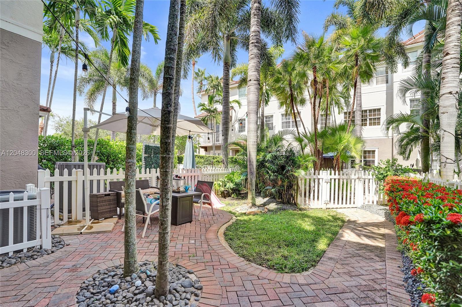 A fenced backyard features a brick patio, a small lawn, and several tall palm trees — 132 Ocean Cay Way, Hypoluxo FL 33462, HYPOLUXO, FL