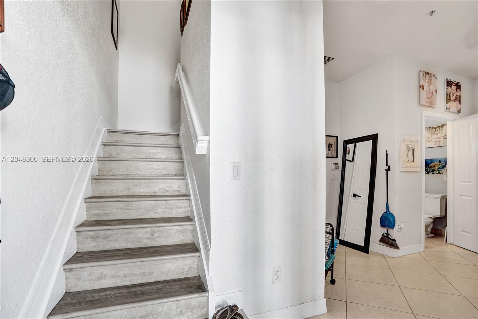 A staircase with light wood-look treads leads upward next to a hallway with a mirror — 132 Ocean Cay Way, Hypoluxo FL 33462, HYPOLUXO, FL