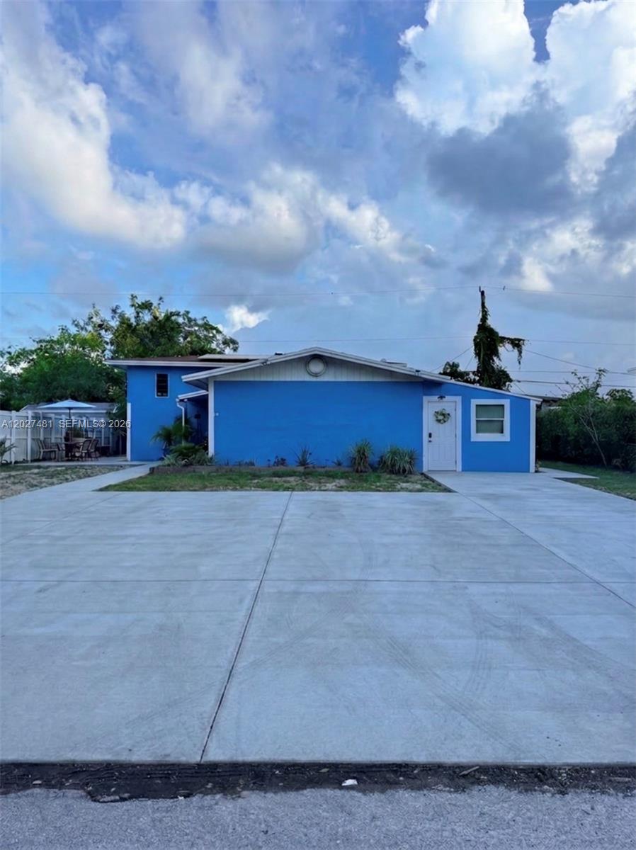 A blue single-story house features a large concrete driveway and a white front door — 1300 NE 203rd St, Miami FL 33179, MIAMI, FL