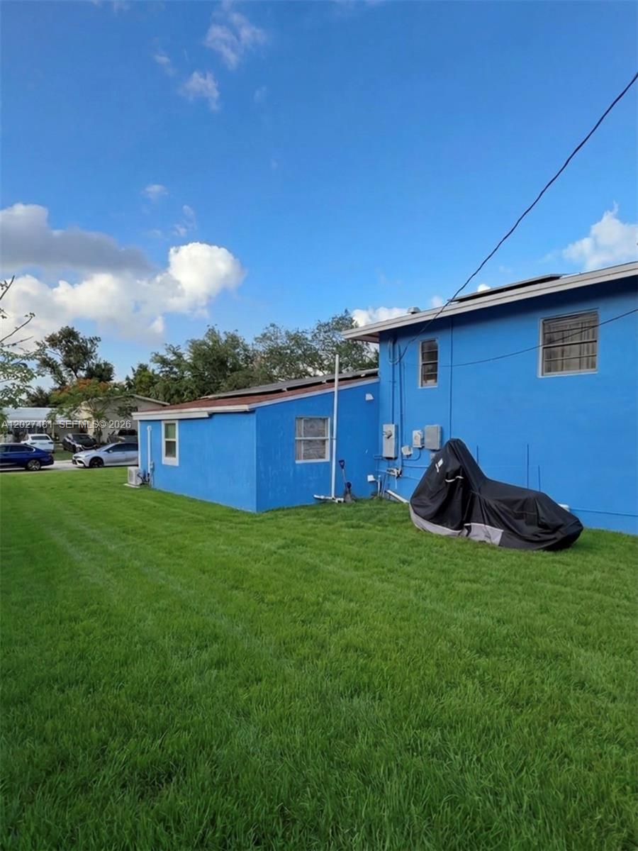 The exterior of a blue house features a grassy lawn and a covered object — 1300 NE 203rd St, Miami FL 33179, MIAMI, FL