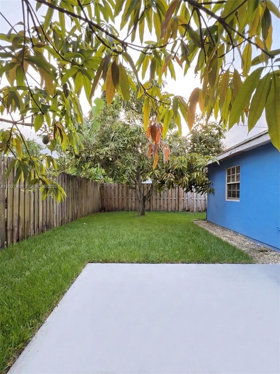 A backyard features a concrete patio, a grassy lawn, a wooden fence, and a tree — 1300 NE 203rd St, Miami FL 33179, MIAMI, FL