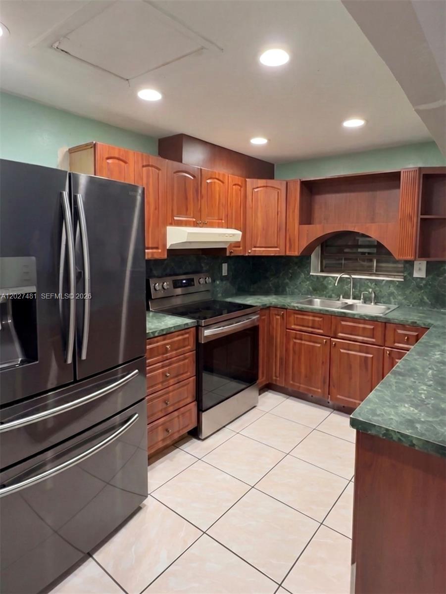 A kitchen features wood cabinets, green countertops, stainless steel appliances, and light-colored floor tiles — 1300 NE 203rd St, Miami FL 33179, MIAMI, FL
