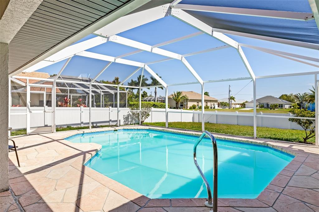 A screened-in swimming pool with a stone patio sits in a backyard with a white fence — 2250 RIO DE JANEIRO AVENUE, PUNTA GORDA, FL