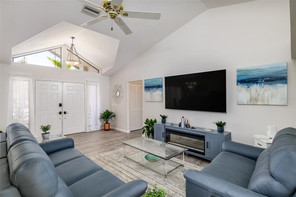 A living room features vaulted ceilings, blue leather sofas, a television, and a fireplace console — 2250 RIO DE JANEIRO AVENUE, PUNTA GORDA, FL