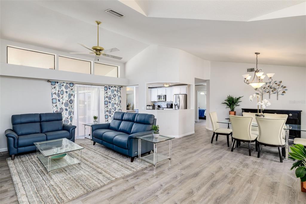 An open-concept living and dining area features vaulted ceilings, blue sofas, and light wood flooring — 2250 RIO DE JANEIRO AVENUE, PUNTA GORDA, FL