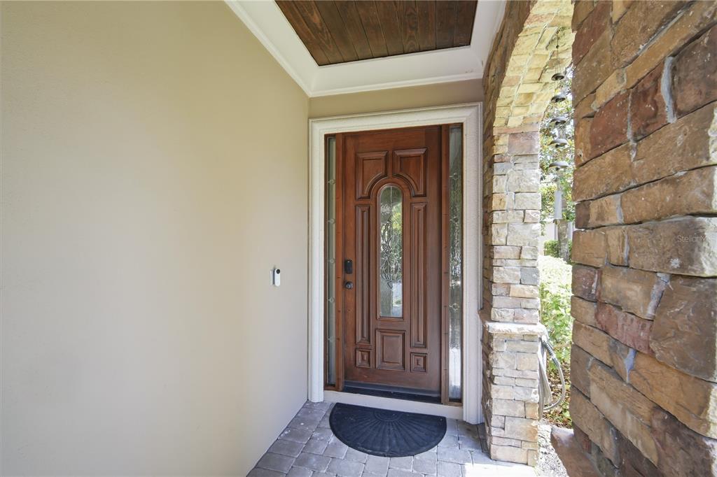 A wooden front door with glass inserts sits under a covered porch with stone accents — 1465 HILLSIDE LANDING DRIVE, TARPON SPRINGS, FL