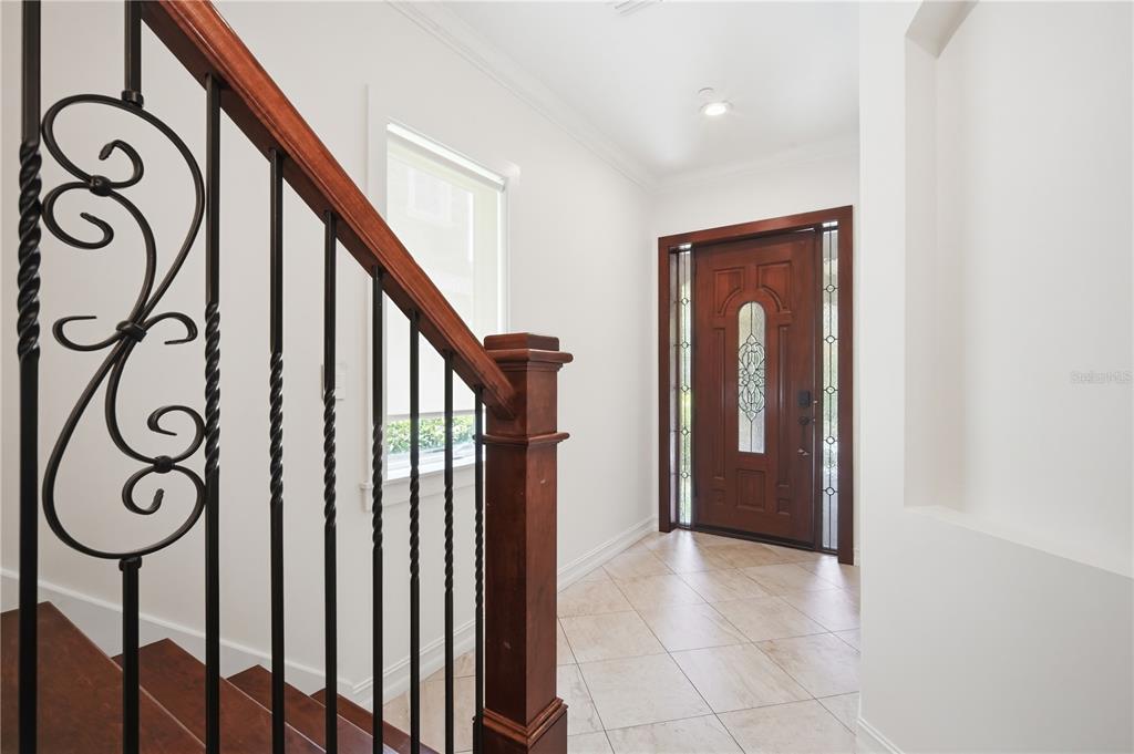 An entryway features a wooden staircase with decorative metal railings, tile flooring, and a front door — 1465 HILLSIDE LANDING DRIVE, TARPON SPRINGS, FL
