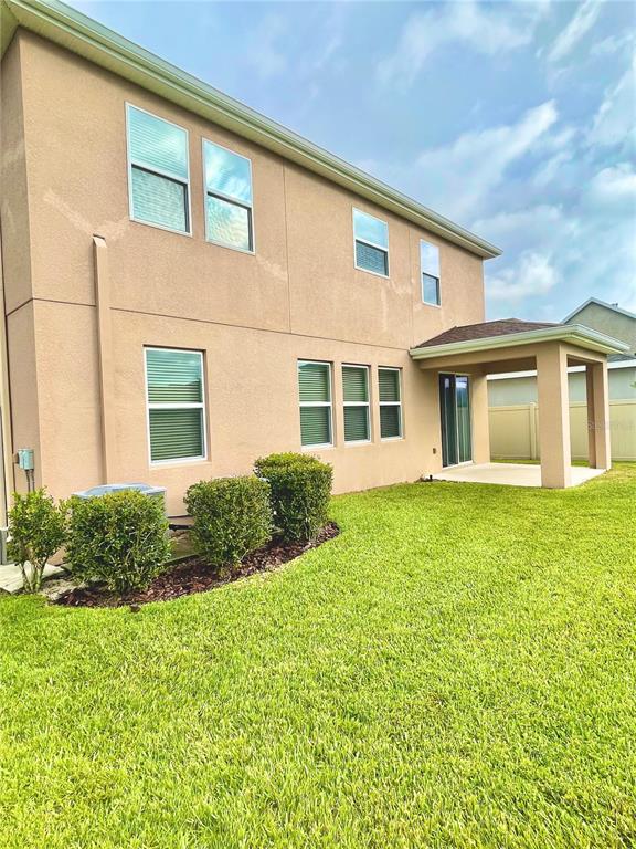 The exterior of a two-story tan stucco house features a covered patio and green lawn — 21648 SOUTHERN CHARM DRIVE, LAND O LAKES, FL