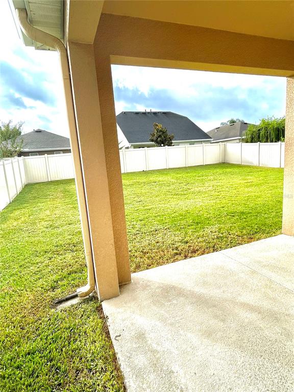A covered concrete patio overlooks a fenced backyard with green grass and neighboring houses — 21648 SOUTHERN CHARM DRIVE, LAND O LAKES, FL