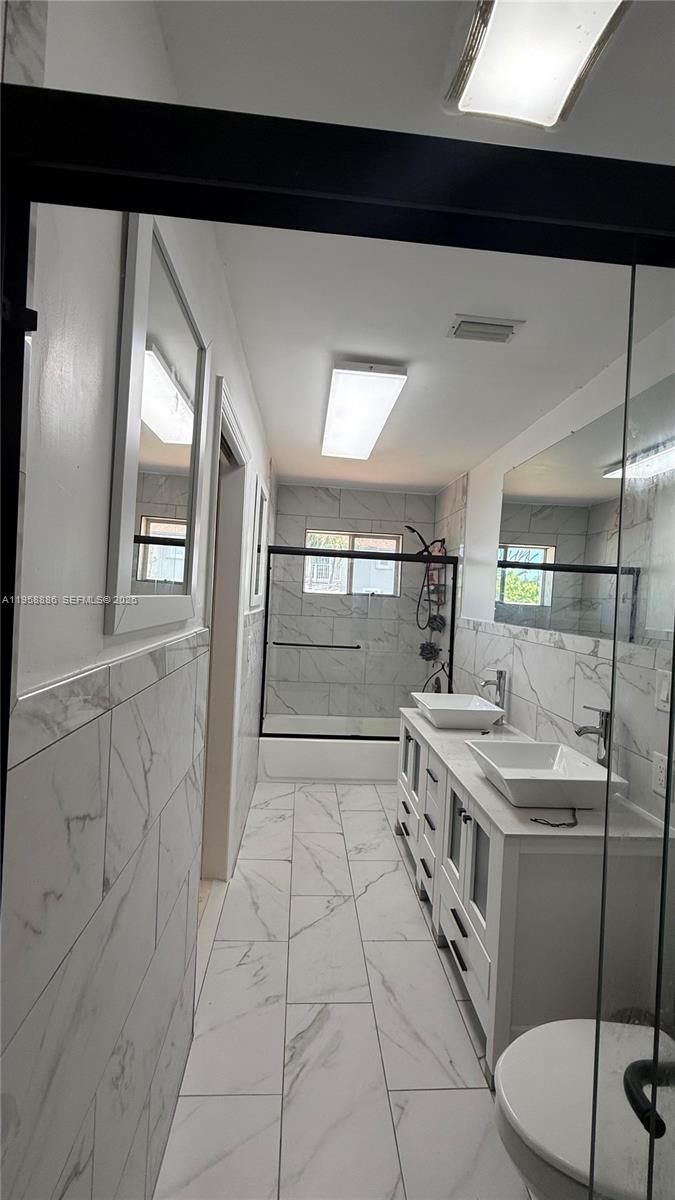 A modern bathroom features a double vanity, marble-look tile, and a glass-enclosed shower — 4465 SW 38th Ter, Dania Beach FL 33312, DANIA BEACH, FL