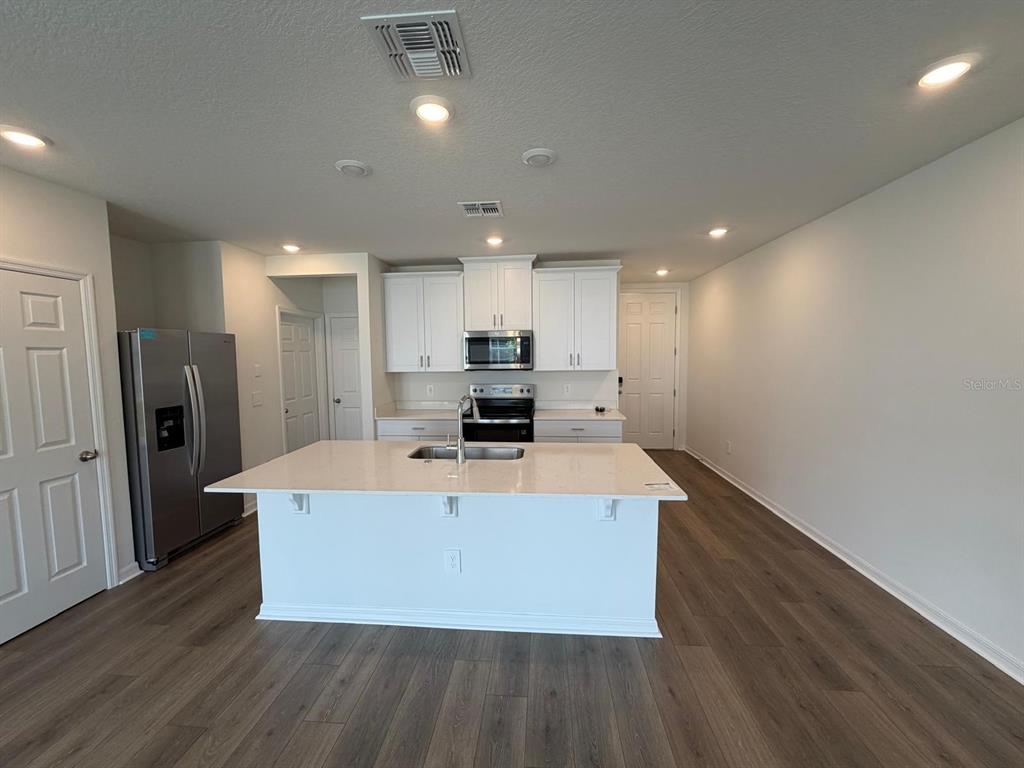 A kitchen features white cabinets, stainless steel appliances, a center island, and wood-look flooring — 4244 RANCH HOUSE ROAD, ST CLOUD, FL