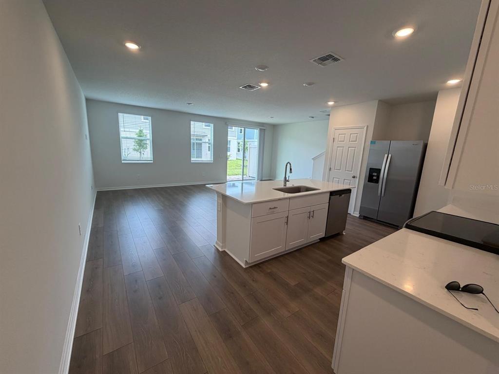 A kitchen with white cabinets and quartz countertops opens to a living area with wood flooring — 4244 RANCH HOUSE ROAD, ST CLOUD, FL
