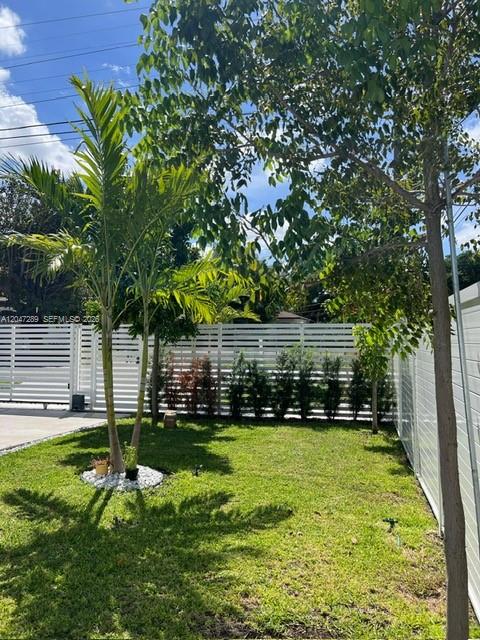 A grassy backyard features a palm tree, a large tree, and white horizontal privacy fencing — 5629 NW 31st Ave, Miami FL 33142, MIAMI, FL