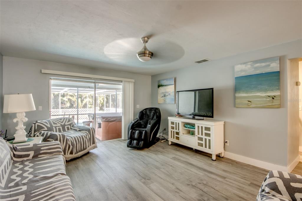 A living room features light wood-look flooring, a massage chair, and a sliding glass door — 912 SE 24TH AVENUE UNIT A &  B, CAPE CORAL, FL