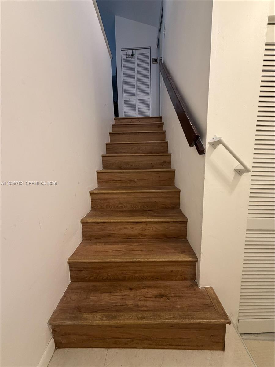 A wooden staircase with a dark handrail leads to a landing with louvered doors — 221 W Park Dr # 3, Miami FL 33172, MIAMI, FL