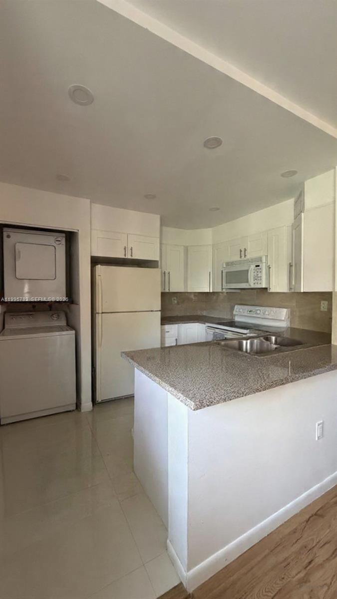 A kitchen features white cabinets, granite countertops, a stainless steel sink, and stacked laundry appliances — 221 W Park Dr # 3, Miami FL 33172, MIAMI, FL