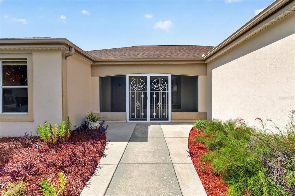 A concrete walkway leads to the front entrance of a house with a screen door — 1911 DEL NORTE DRIVE, THE VILLAGES, FL